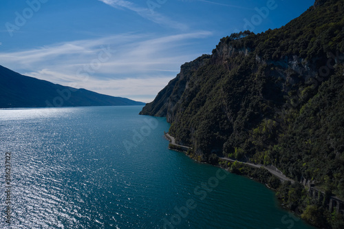 Rough rocky stones. Red rocks on a blue background. Gray rocky slopes in the water. Alps part on blue sky. Aerial view of the big rocks of Lake Garda, Italy.