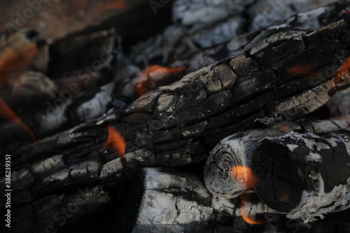 Smoldered logs burned in vivid fire close up. Atmospheric background with flame of campfire. Unimaginable detailed image of bonfire from inside with copy space. Whirlwind of smoke and glowing embers.
