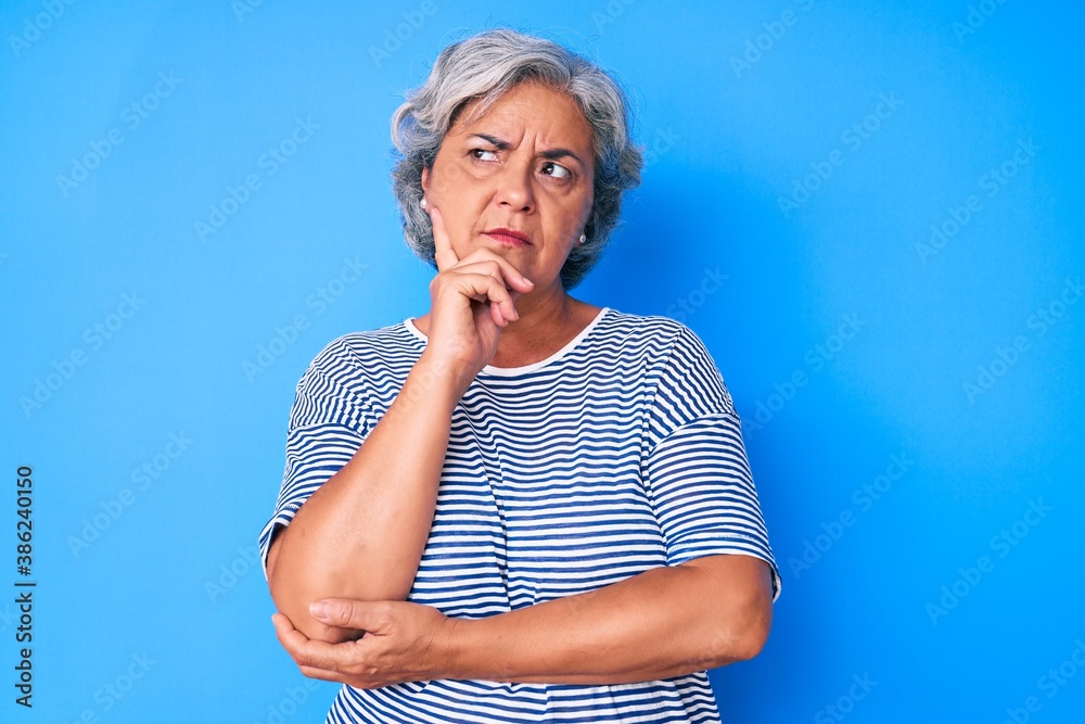 Senior hispanic grey- haired woman wearing casual clothes serious face thinking about question with hand on chin, thoughtful about confusing idea Senior hispanic grey- haired woman wearing casual clothes serious face thinking about question with hand on chin, thoughtful about confusing idea
