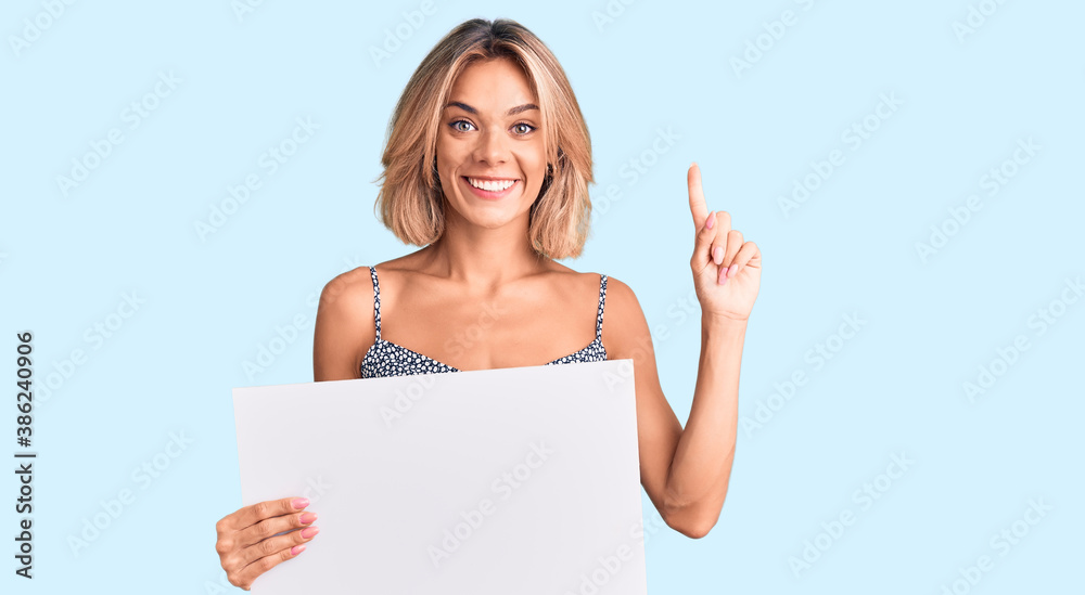 Beautiful caucasian woman holding blank empty banner surprised with an idea or question pointing finger with happy face, number one Beautiful caucasian woman holding blank empty banner surprised with an idea or question pointing finger with happy face, number one