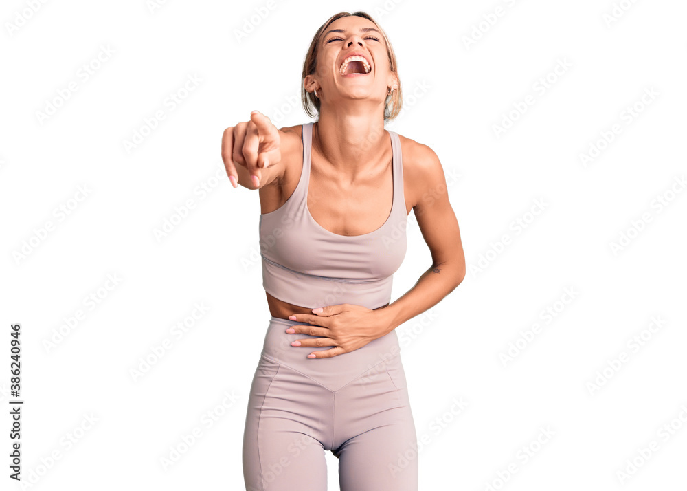 Beautiful caucasian woman wearing sportswear laughing at you, pointing finger to the camera with hand over body, shame expression