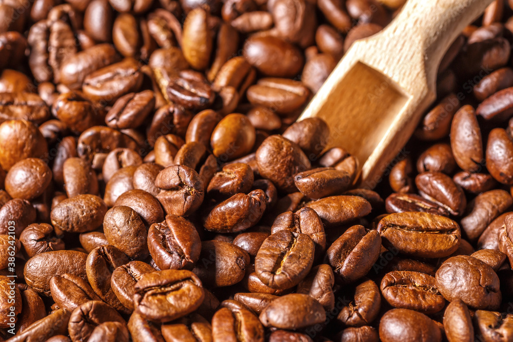Fototapeta premium Freshly roasted coffee beans background.Dark roasted coffee beans with scoop on wooden background.