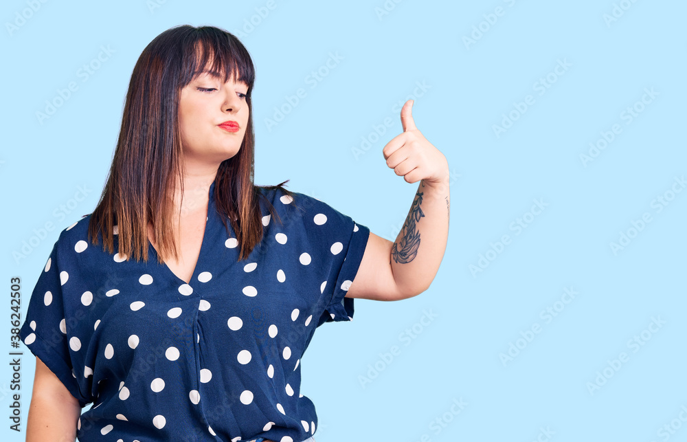 Young plus size woman wearing casual clothes looking proud, smiling doing thumbs up gesture to the side Young plus size woman wearing casual clothes looking proud, smiling doing thumbs up gesture to the side