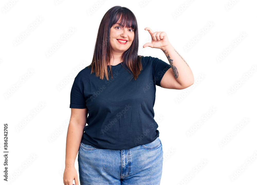 Young plus size woman wearing casual clothes smiling and confident gesturing with hand doing small size sign with fingers looking and the camera. measure concept. Young plus size woman wearing casual clothes smiling and confident gesturing with hand doing small size sign with fingers looking and the camera. measure concept.