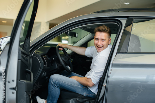 A young man is sitting in the cabin of a new car and testing it. Buying a car © Andrii