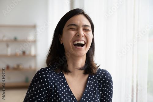 Close up of overjoyed young asian woman laugh at good funny joke indoors. Happy smiling millennial Vietnamese female have fun talking communicating, show optimism and happiness. Humor concept.