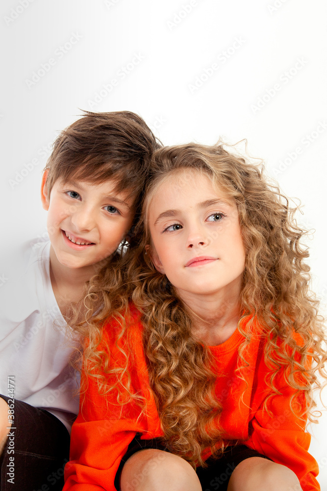 curly haired girl in an orange long sleeve t-shirt sits next to her friend in a white t-shirt