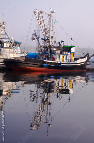 Colorful, weathered fishing boat in a marina on a foggy day
