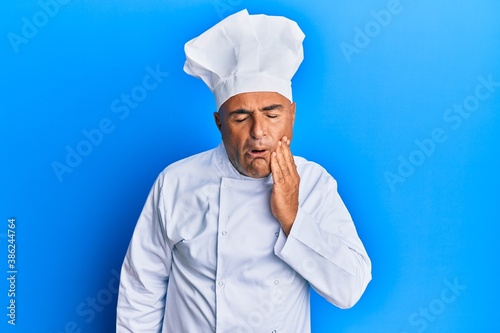Mature middle east man wearing professional cook uniform and hat touching mouth with hand with painful expression because of toothache or dental illness on teeth. dentist