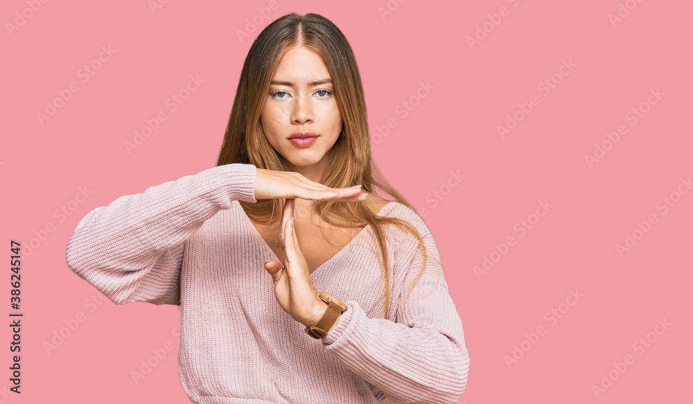 Beautiful blonde woman wearing casual winter pink sweater doing time out gesture with hands, frustrated and serious face Beautiful blonde woman wearing casual winter pink sweater doing time out gesture with hands, frustrated and serious face