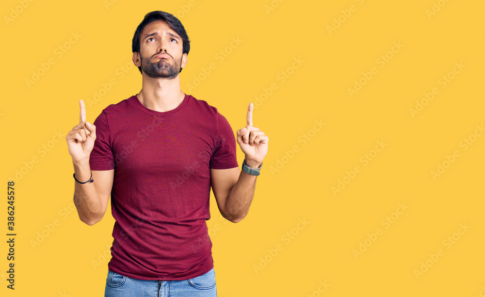 Handsome hispanic man wearing casual clothes pointing up looking sad and upset, indicating direction with fingers, unhappy and depressed. Handsome hispanic man wearing casual clothes pointing up looking sad and upset, indicating direction with fingers, unhappy and depressed.