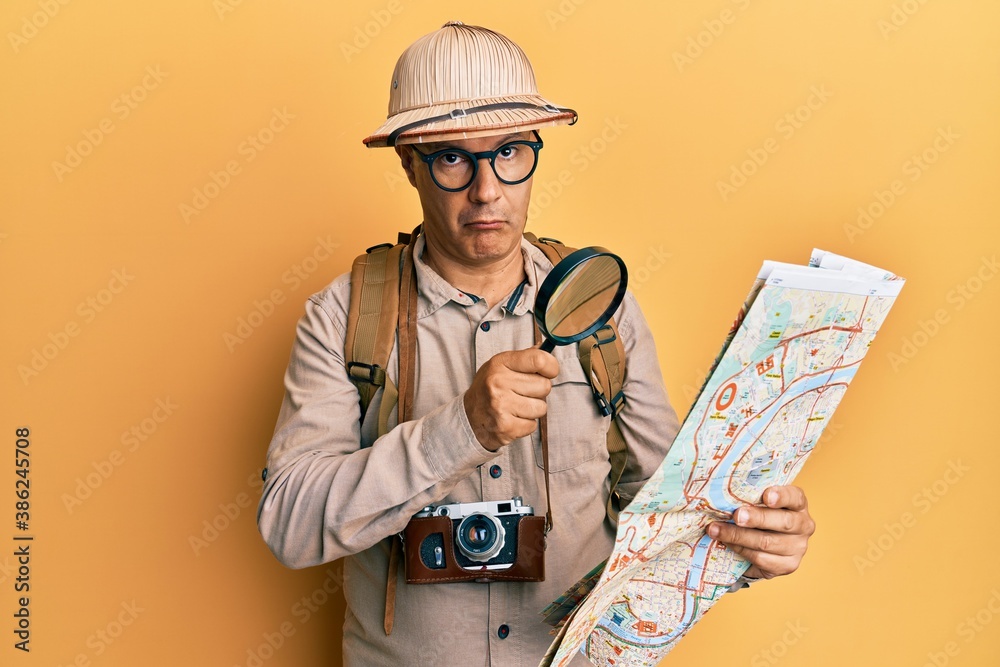Middle age bald man wearing explorer hat holding magnifying glass on a map depressed and worry for distress, crying angry and afraid. sad expression.