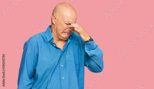 Middle age bald man wearing casual clothes smelling something stinky and disgusting, intolerable smell, holding breath with fingers on nose. bad smell