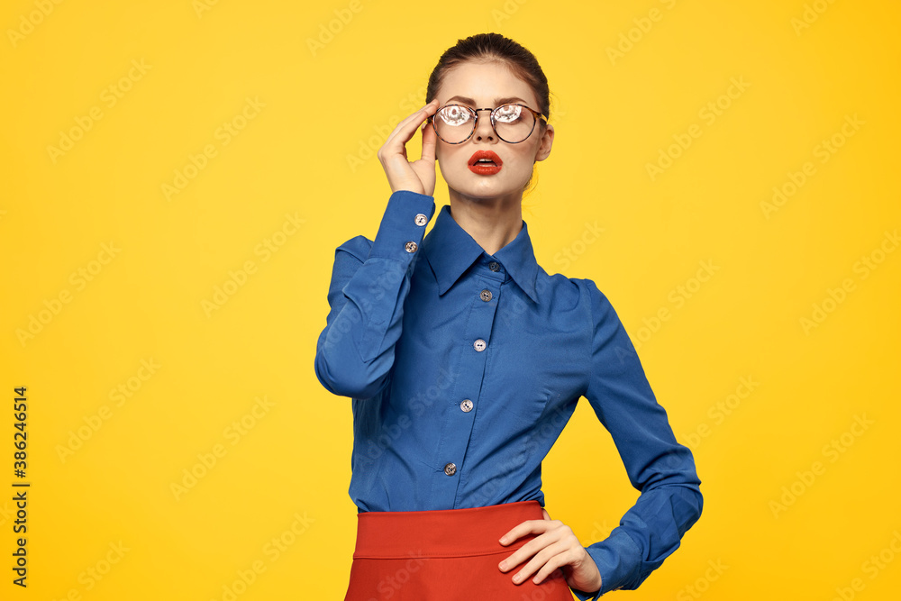 Woman in blue shirt and red skirt glasses on face confident look portrait yellow background cropped view