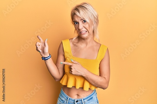 Young blonde girl wearing casual clothes pointing aside worried and nervous with both hands  concerned and surprised expression