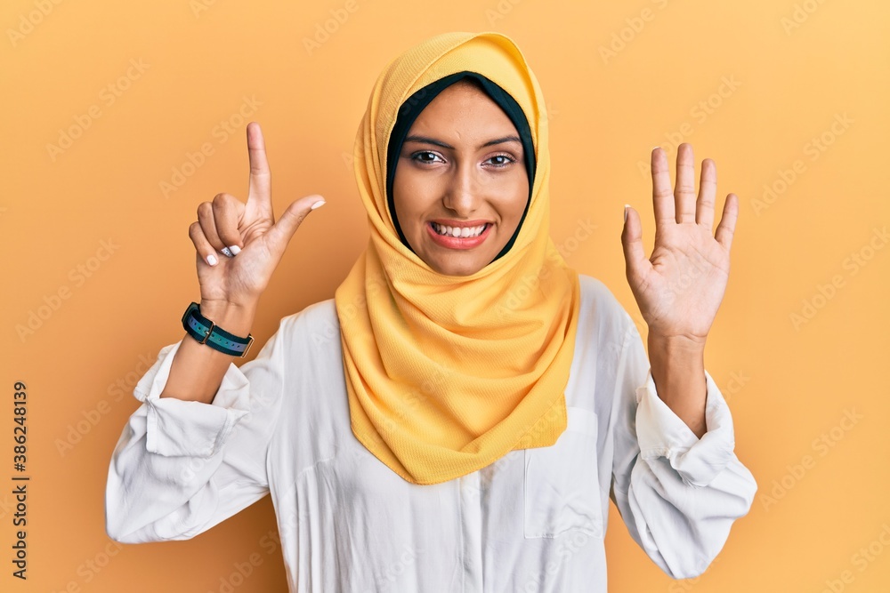 Young brunette arab woman wearing traditional islamic hijab scarf showing and pointing up with fingers number seven while smiling confident and happy.