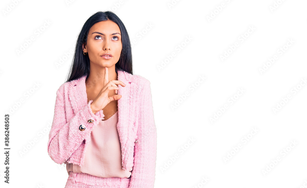 Young beautiful latin girl wearing business clothes thinking concentrated about doubt with finger on chin and looking up wondering Young beautiful latin girl wearing business clothes thinking concentrated about doubt with finger on chin and looking up wondering