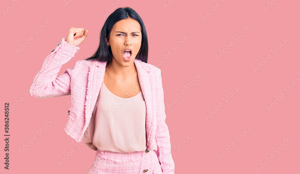 Young beautiful latin girl wearing business clothes angry and mad raising fist frustrated and furious while shouting with anger. rage and aggressive concept. Young beautiful latin girl wearing business clothes angry and mad raising fist frustrated and furious while shouting with anger. rage and aggressive concept.