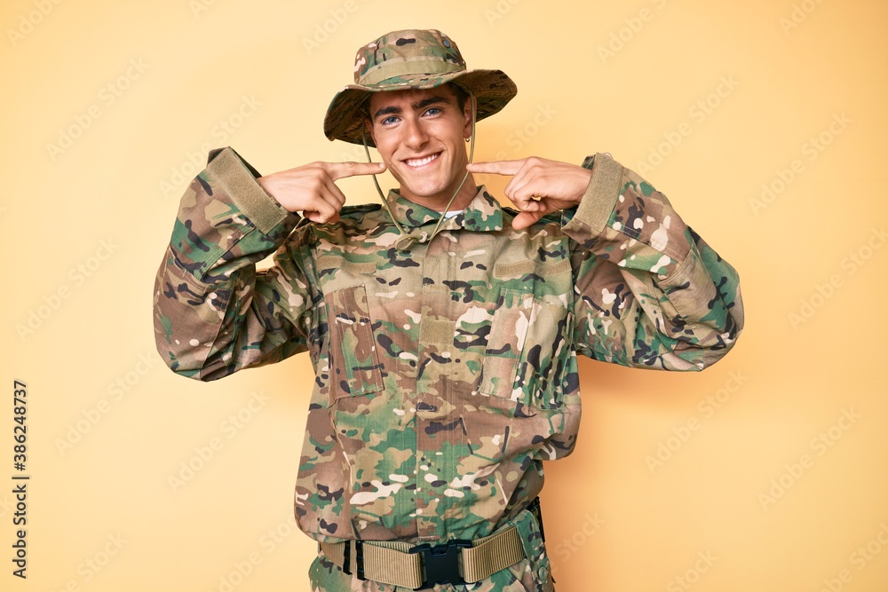 Young handsome man wearing camouflage army uniform smiling cheerful showing and pointing with fingers teeth and mouth. dental health concept.