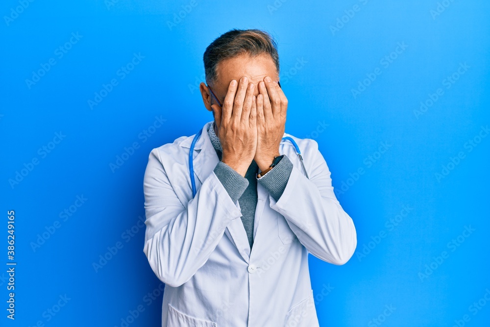 Handsome middle age man wearing doctor uniform and stethoscope with sad expression covering face with hands while crying. depression concept. Handsome middle age man wearing doctor uniform and stethoscope with sad expression covering face with hands while crying. depression concept.