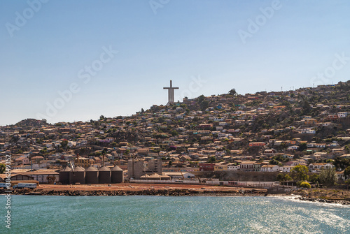 Coquimbo, Chile - December 7, 2008: Tall Millennium Cross Trinity surrounded by houses in different colors under blownish cloudscape towers over harbor site and azure ocean water.. photo