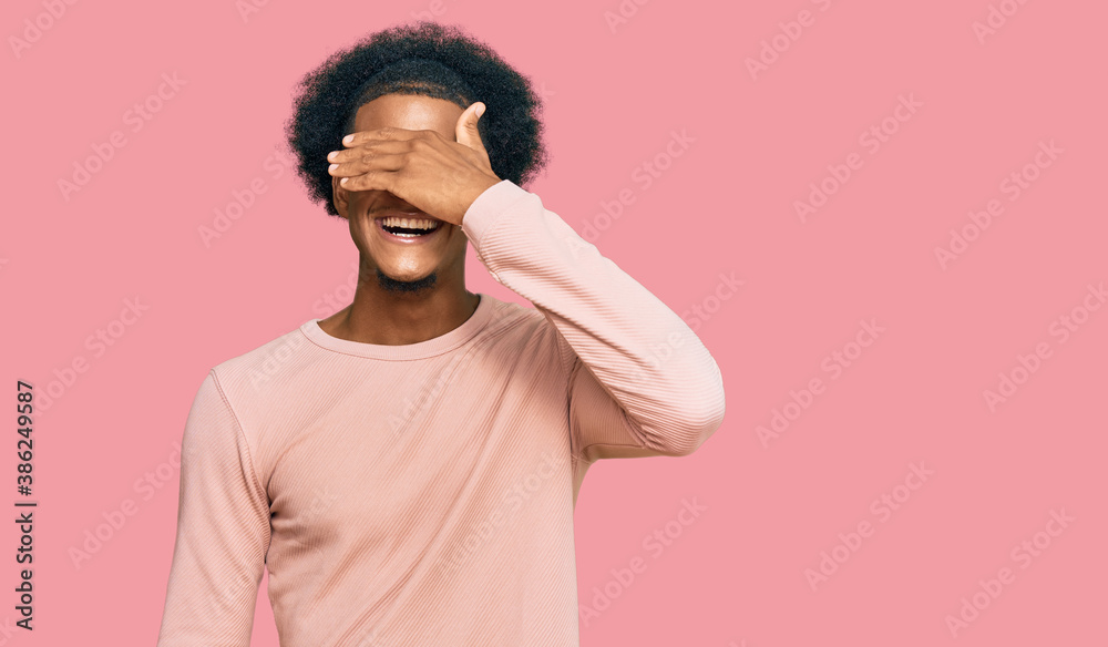 African american man with afro hair wearing casual clothes smiling and laughing with hand on face covering eyes for surprise. blind concept. African american man with afro hair wearing casual clothes smiling and laughing with hand on face covering eyes for surprise. blind concept.