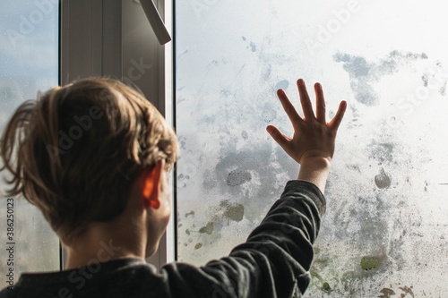 A little boy draws on a fogged, wet window