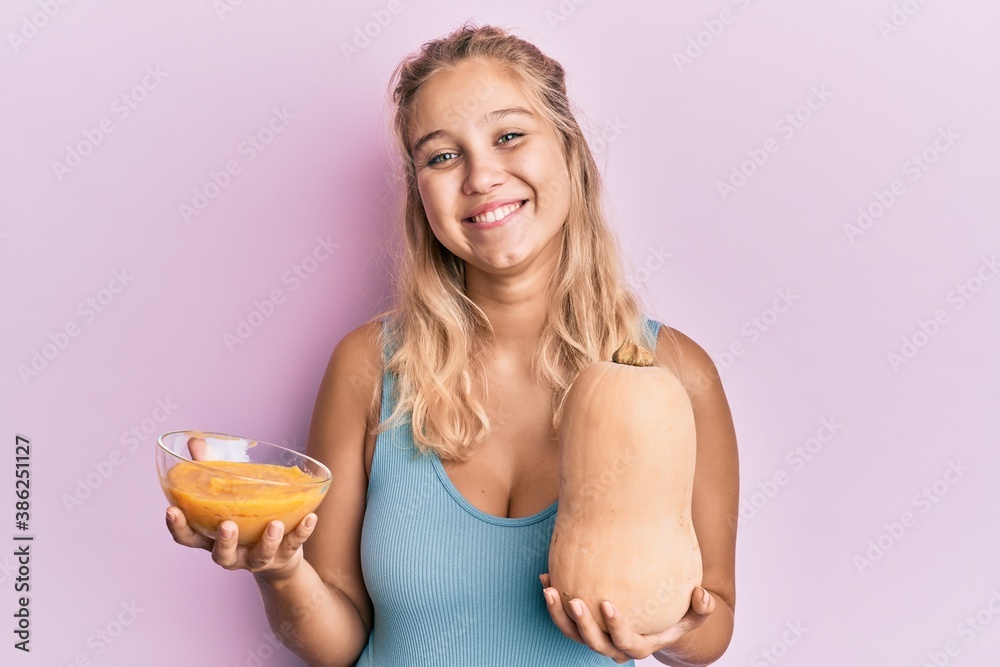 Young blonde girl holding fresh pumpkin and soup smiling with a happy and cool smile on face. showing teeth. Young blonde girl holding fresh pumpkin and soup smiling with a happy and cool smile on face. showing teeth.