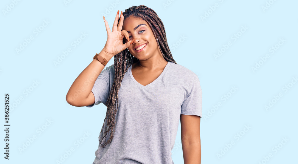 Young african american woman with braids wearing casual clothes smiling happy doing ok sign with hand on eye looking through fingers Young african american woman with braids wearing casual clothes smiling happy doing ok sign with hand on eye looking through fingers