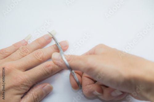 Hand with nail scissors cuts long nails on a woman's hand in the process of cutting nails close up on a white background. Manicure and fingernail trimming isolated