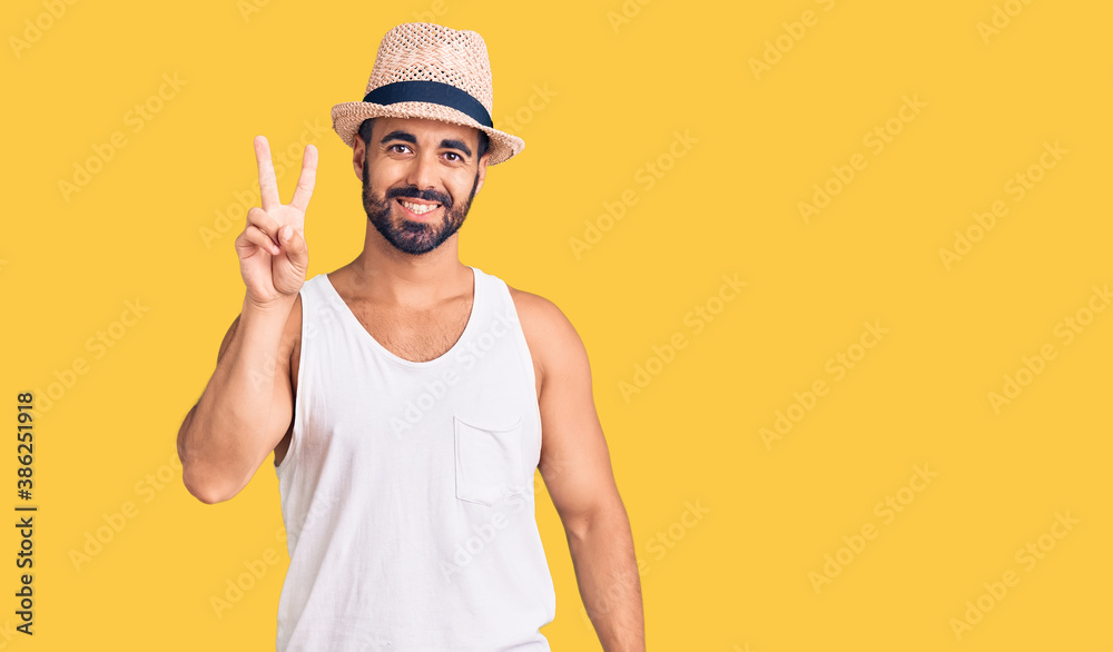 Naklejka premium Young hispanic man wearing casual summer hat showing and pointing up with fingers number two while smiling confident and happy.