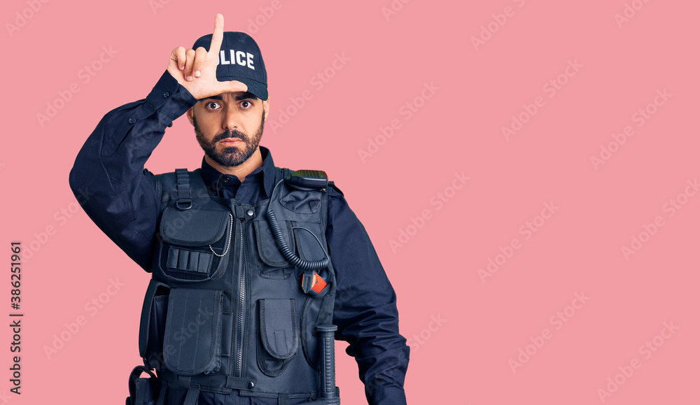 Young hispanic man wearing police uniform making fun of people with fingers on forehead doing loser gesture mocking and insulting. Young hispanic man wearing police uniform making fun of people with fingers on forehead doing loser gesture mocking and insulting.