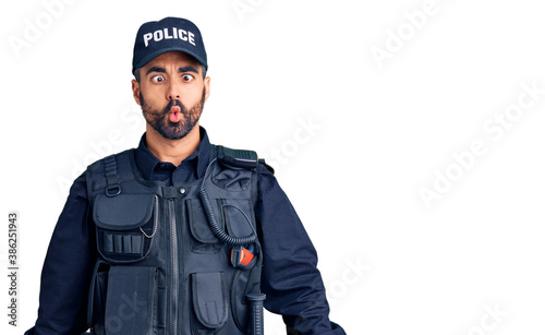 Young hispanic man wearing police uniform making fish face with lips, crazy and comical gesture. funny expression. photo