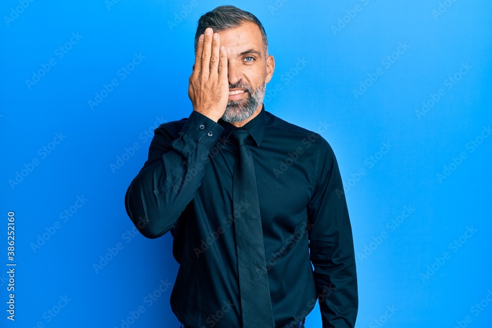 Middle age handsome man wearing business shirt and tie covering one eye with hand, confident smile on face and surprise emotion.