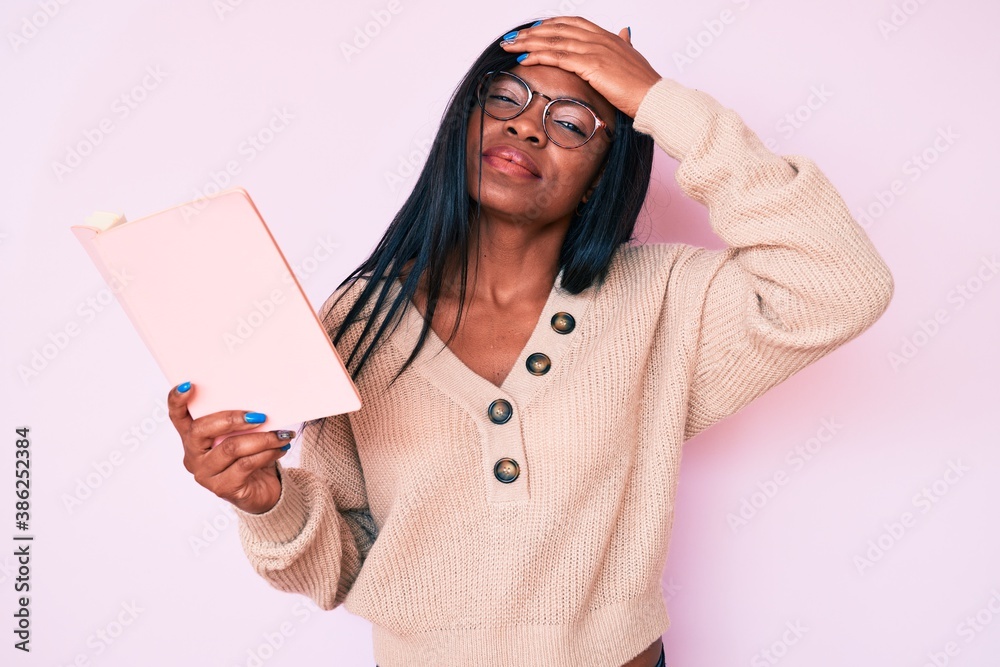 Young african american woman wearing glasses holding book stressed and frustrated with hand on head, surprised and angry face Young african american woman wearing glasses holding book stressed and frustrated with hand on head, surprised and angry face
