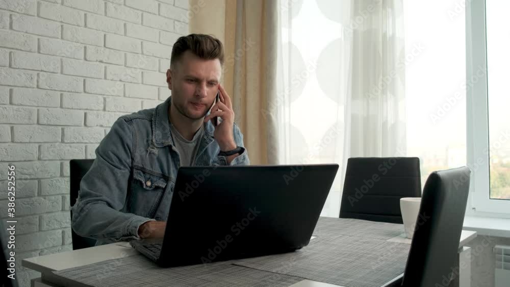 A handsome man freelancer is sitting at a laptop and talking on the phone. Trading on the stock exchange. Businessman. Work at home A handsome man freelancer is sitting at a laptop and talking on the phone. Trading on the stock exchange. Businessman. Work at home
