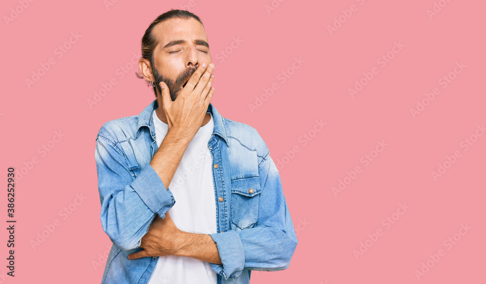 Attractive man with long hair and beard wearing casual denim jacket bored yawning tired covering mouth with hand. restless and sleepiness.