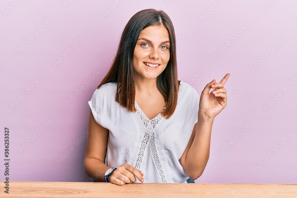 Young caucasian woman wearing casual clothes sitting on the table smiling happy pointing with hand and finger to the side Young caucasian woman wearing casual clothes sitting on the table smiling happy pointing with hand and finger to the side