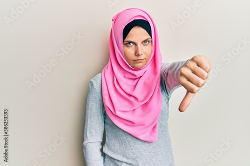 Young caucasian woman wearing traditional islamic hijab scarf looking unhappy and angry showing rejection and negative with thumbs down gesture. bad expression. © Krakenimages.com