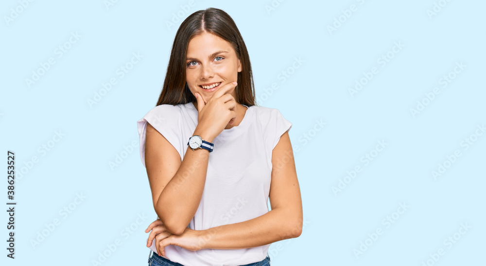 Young caucasian woman wearing casual white tshirt looking confident at the camera smiling with crossed arms and hand raised on chin. thinking positive. Young caucasian woman wearing casual white tshirt looking confident at the camera smiling with crossed arms and hand raised on chin. thinking positive.