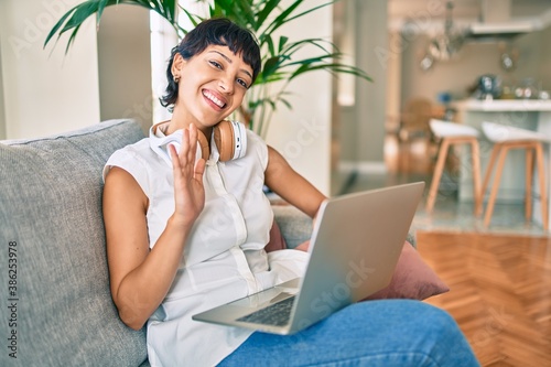 Beautiful brunette woman with short hair at home doing video conference waving at computer