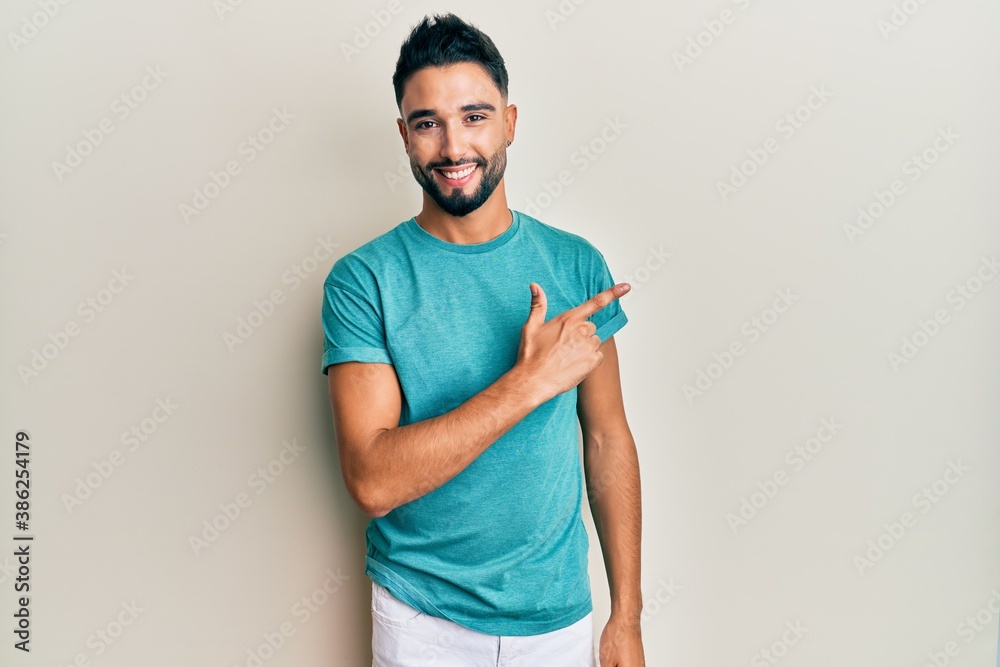 Young man with beard wearing casual clothes smiling cheerful pointing with hand and finger up to the side Young man with beard wearing casual clothes smiling cheerful pointing with hand and finger up to the side