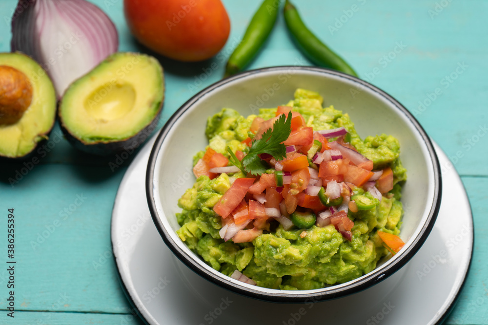 Mexican guacamole with chili pepper and tomato on turquoise background Mexican guacamole with chili pepper and tomato on turquoise background