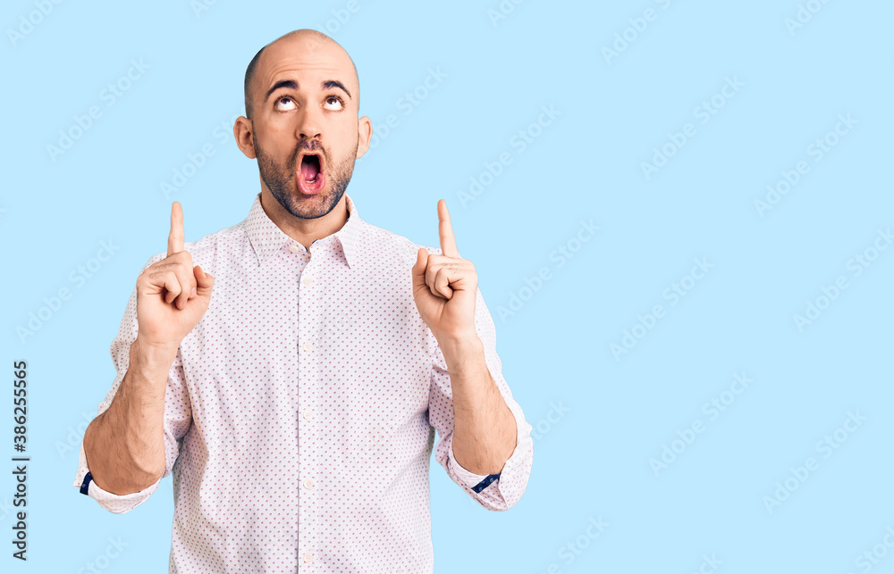 Naklejka premium Young handsome man wearing elegant shirt amazed and surprised looking up and pointing with fingers and raised arms.