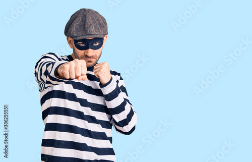 Young handsome man wearing burglar mask punching fist to fight, aggressive and angry attack, threat and violence © Krakenimages.com