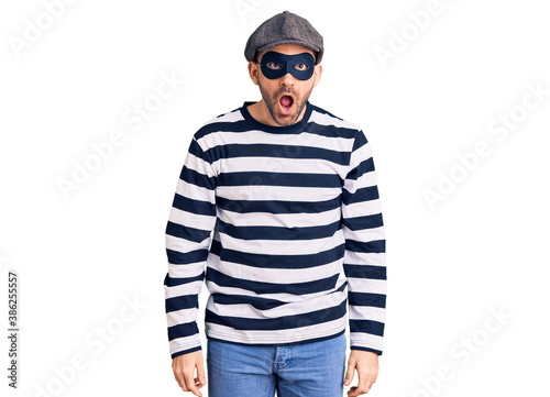 Young handsome man wearing burglar mask afraid and shocked with surprise and amazed expression, fear and excited face. © Krakenimages.com