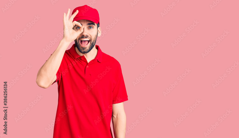 Young handsome man with beard wearing delivery uniform doing ok gesture with hand smiling, eye looking through fingers with happy face. Young handsome man with beard wearing delivery uniform doing ok gesture with hand smiling, eye looking through fingers with happy face.