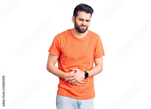 Young handsome man with beard wearing casual t-shirt with hand on stomach because indigestion, painful illness feeling unwell. ache concept.