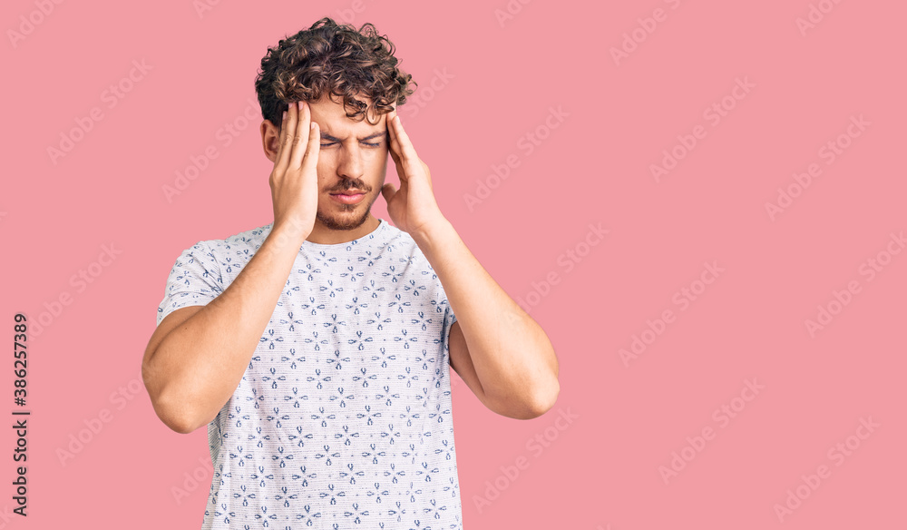 Young handsome man with curly hair wearing casual clothes suffering from headache desperate and stressed because pain and migraine. hands on head. Young handsome man with curly hair wearing casual clothes suffering from headache desperate and stressed because pain and migraine. hands on head.