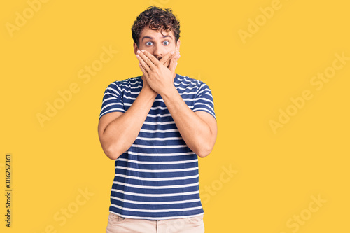 Young handsome man with curly hair wearing casual clothes shocked covering mouth with hands for mistake. secret concept.